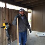 A man in a gray jacket working with a tool in a partially constructed interior for plumbing and HVAC projects.