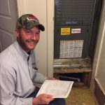 Smiling technician reading a maintenance manual beside an HVAC unit at The Darville Company.